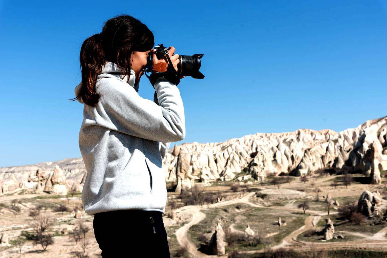 Side view of photographer woman taking shot of hills in sunny day in Cappadocia, Turkey.